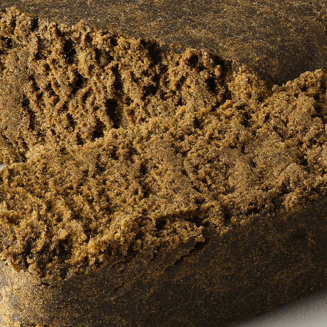 Premium CBD Hash Block – Pure Botanica Traditional Hemp Hash Close-up of a premium CBD hash block with a freshly cut piece revealing its soft, crumbly texture. High-quality hemp hash crafted from CBD-rich cannabis, ideal for customers seeking authentic traditional hash with natural aroma and premium quality.