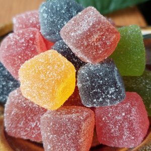 STARTSEITE Whole Circle Farms CBD vegane Gummibonbons in einer Flasche neben einer Auswahl bunter CBD-Gummibonbons auf einem Holztisch.